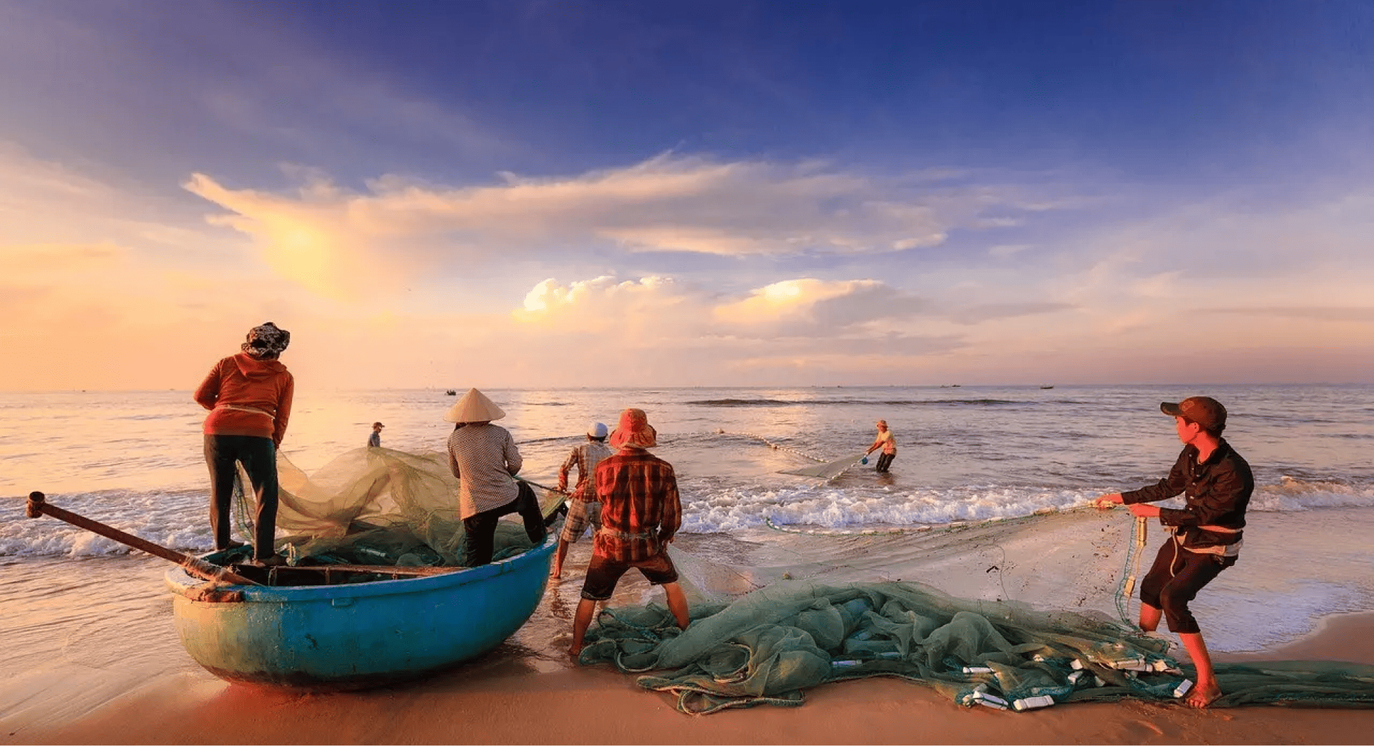 Fishermen on a beach pulling in a boat at sunset